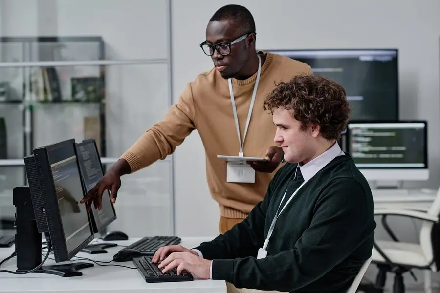 Black IT support technician helping an office worker troubleshoot a workstation